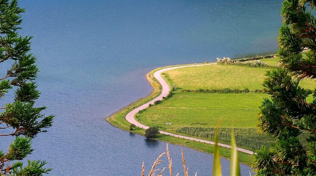 Narrow road winding along the green shore of a crater lake in São Miguel, Azores