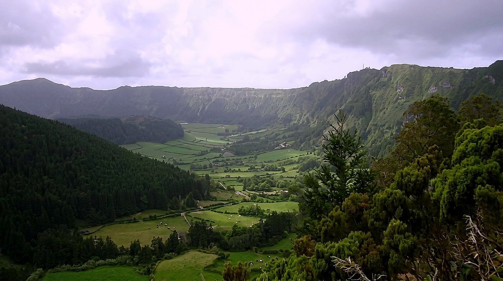 Misty caldera rim view, forested slopes framing the grassy valley floor of Sete Cidades
