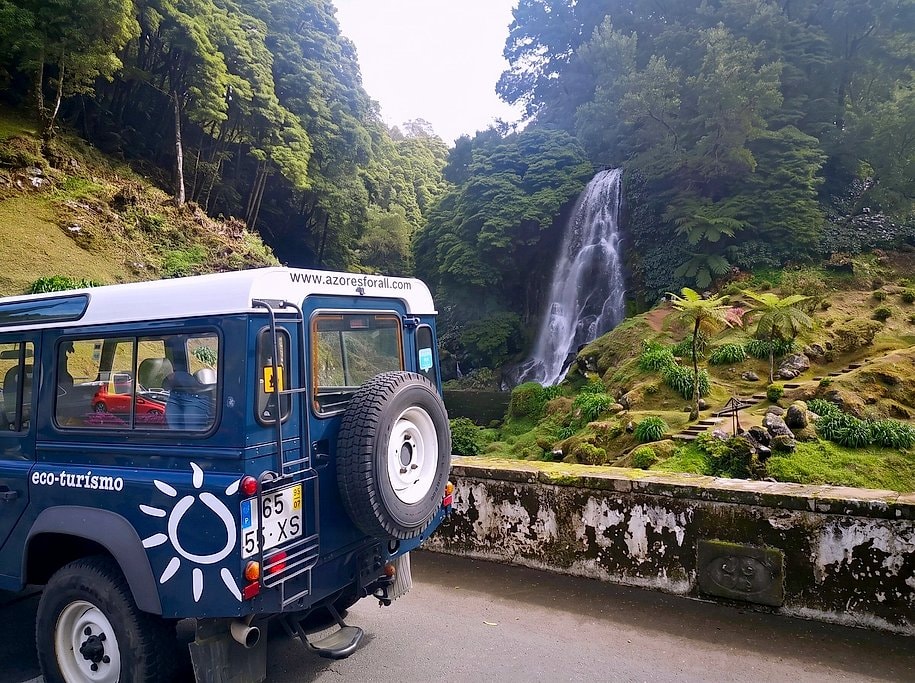 4x4 jeep parked beside the tall cascading waterfall at Ribeira dos Caldeirões park