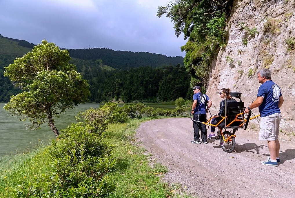 Guides pause the Joelette chair so the rider can take in cliffside views over Sete Cidades lake.