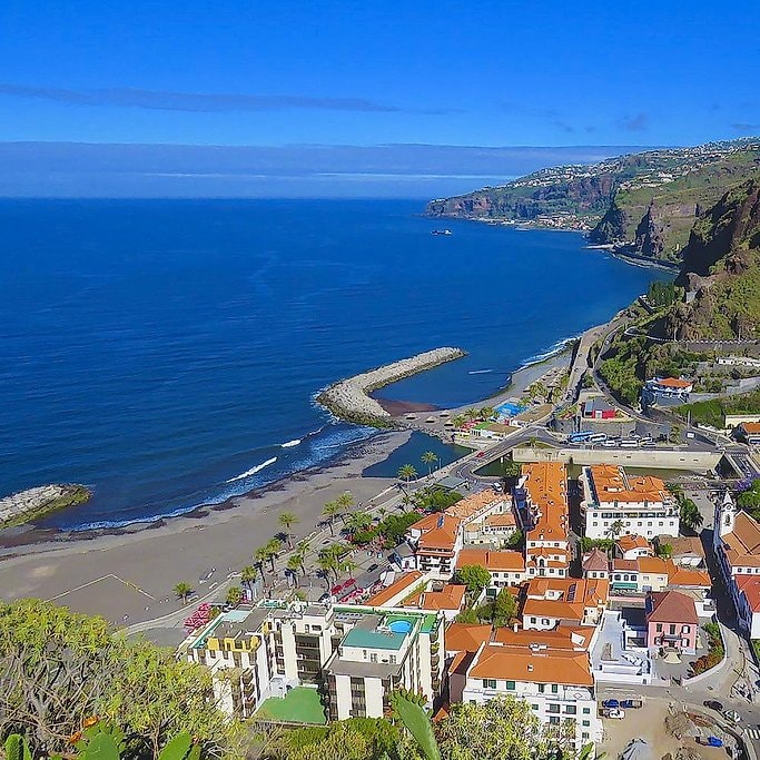 Aerial view of a Madeira coastal town with orange rooftops and a curved breakwater.