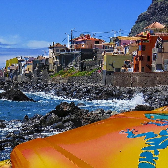 Colorful houses along Madeira's black volcanic coastline, waves breaking on the rocks below.