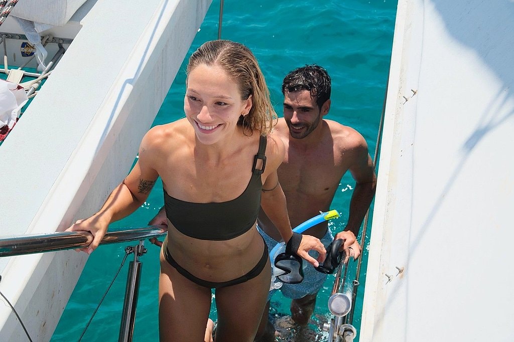 Smiling couple climbing the swim ladder back aboard holding snorkeling gear.