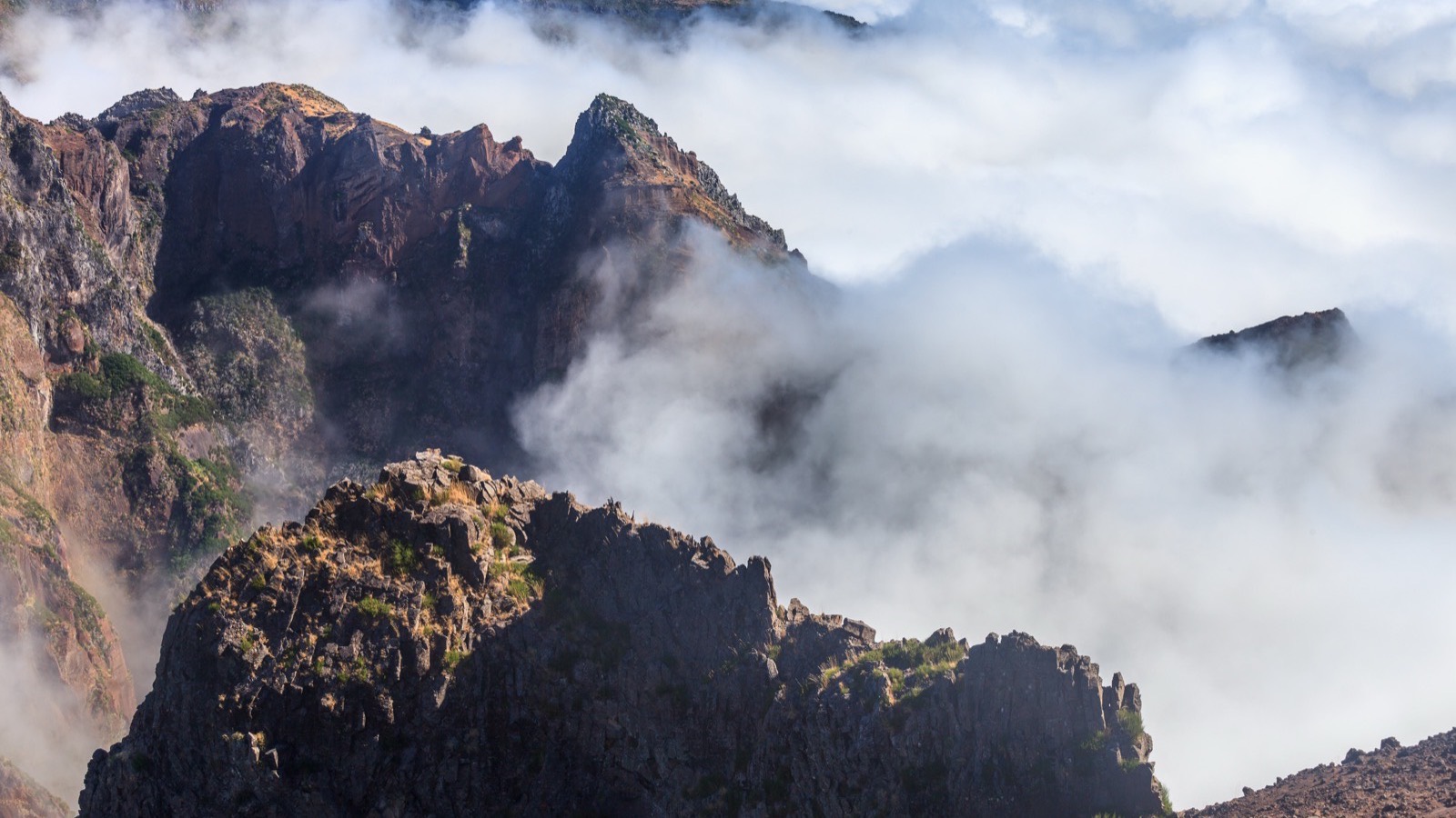 マデイラ島Pico do Arieiro周辺の岩肌がむき出しの山頂が、厚い雲海の上に朝日を浴びてそびえ立つ様子。